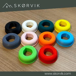 Könnte beinhalten: Eine Sammlung von zehn kreisförmigen, ringförmigen Silikonabdeckungen in verschiedenen Unifarben, darunter Schwarz, Weiß, Dunkelblaugrün, Gelb, Grau, Hellrosa, Orange, Blau, Hellgrün und Rot, jeweils mit einer zentralen Öffnung mit flacher Kante.