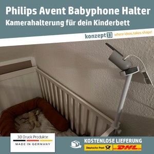 Puede incluir: Un soporte blanco para babyphone con una abrazadera blanca unida a una cuna. El soporte está hecho de plástico impreso en 3D y está diseñado para sujetar una cámara de babyphone. El texto "3D Druck Produkte MADE IN GERMANY" es visible en la parte inferior de la imagen.