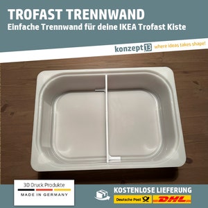 Op de afbeelding: Een witte plastic scheidingswand voor een Trofast opbergdoos. De scheidingswand is ontworpen om twee aparte compartimenten in de doos te creëren. De tekst "TROFAST TRENNWAND" en "Einfache Trennwand für deine IKEA Trofast Kiste" staat bovenaan de afbeelding.