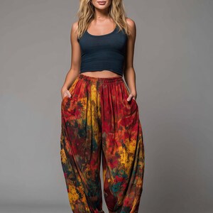 May include: A woman wearing a navy blue tank top and vibrant tie-dye harem pants. The pants feature a mix of red, yellow, and green hues. The pants have pockets and a comfortable, loose fit.