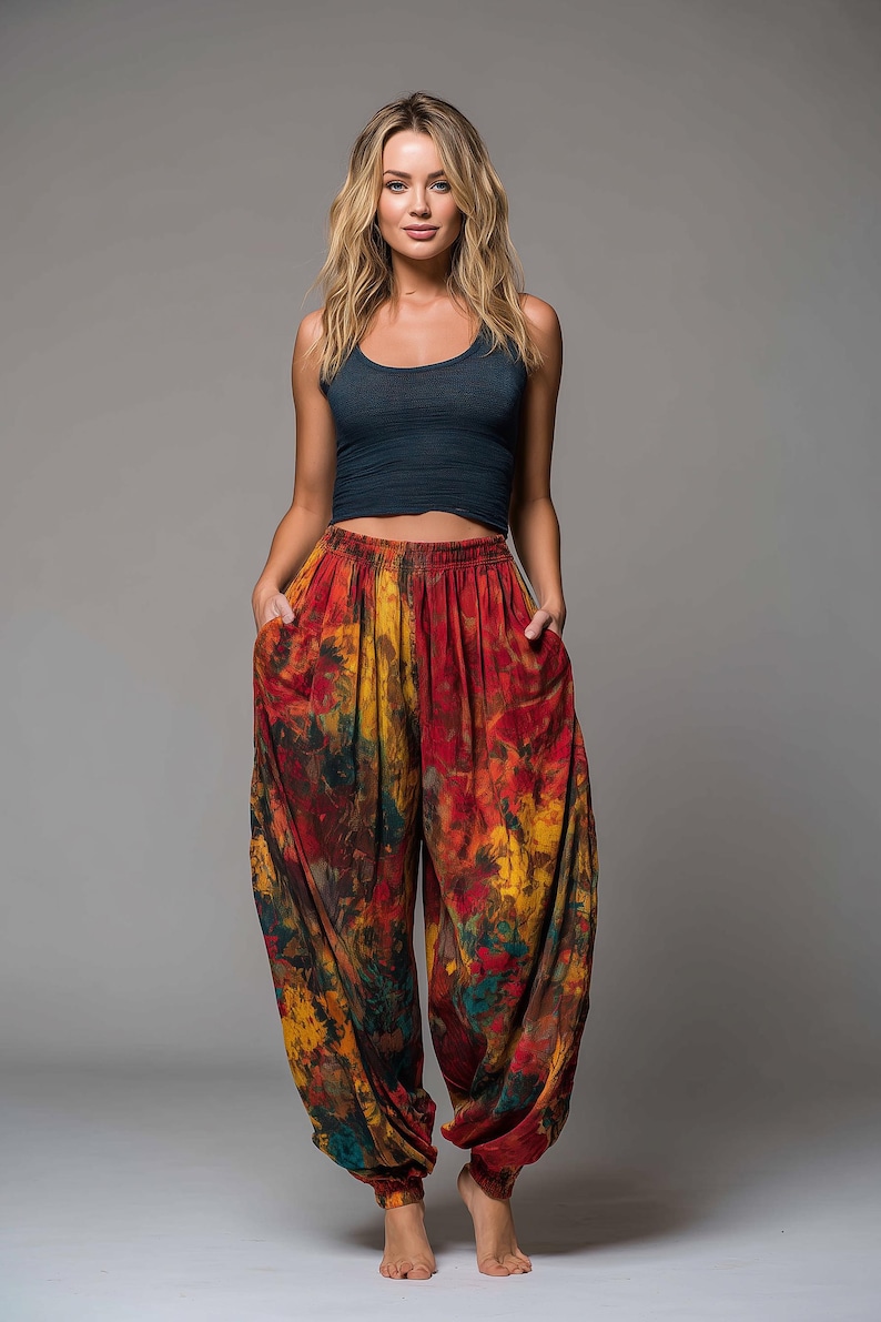 May include: A woman wearing a navy blue tank top and vibrant tie-dye harem pants. The pants feature a mix of red, yellow, and green hues. The pants have pockets and a comfortable, loose fit.