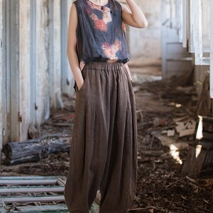 May include: A woman wearing a brown sleeveless top with a floral print and brown wide-leg pants. She is standing in a room with a wooden floor and white walls.
