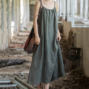 May include: A sage green, sleeveless dress with thin straps. The dress has a loose, flowing fit and reaches mid-calf. A brown shoulder bag is worn over the shoulder. The dress is made of a textured fabric.