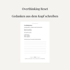 Könnte beinhalten: Ein weißes Notizbuch mit dem Titel "Overthinking Reset" und deutschem Text. Das Innere des Notizbuchs hat linierte Seiten und weiteren deutschen Text, der den Benutzer ermutigt, seine Gedanken aufzuschreiben.