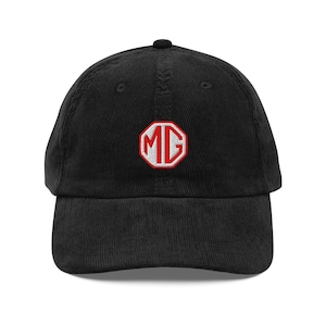 Puede incluir: Gorra de béisbol de pana negra con el logotipo MG bordado en rojo y blanco. La gorra tiene una visera curva y una correa ajustable. Un accesorio clásico para los entusiastas de los coches.