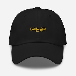 Puede incluir: Gorra de béisbol negra con la palabra "California" bordada en amarillo en cursiva en la parte delantera.