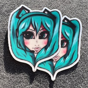 May include: Two stickers featuring a cartoon anime character with long turquoise hair, wearing a headset and a white shirt. The character has large blue eyes and a pink blush on her cheeks.