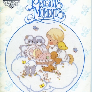 Puede incluir: Diseño de punto de cruz que presenta a un bebé en una cuna sobre una nube, rodeado de ángeles, corderos y mariposas. El diseño está enmarcado por un círculo azul, con las palabras "Precious Moments" en la parte superior. El diseño es de Gloria & Pat.