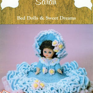 May include: A vintage doll named "Sarah" wearing a blue crocheted dress and hat with floral accents. The doll is set against a pink background, with the text "Bed Dolls & Sweet Dreams" and "Free Gift Tags" visible.