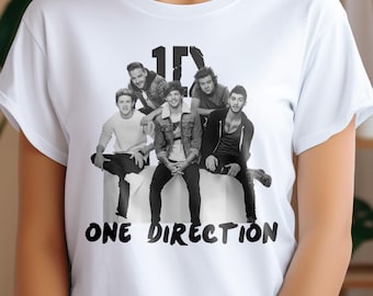 May include: White t-shirt with a black and white image of the band One Direction. The band members are all wearing casual clothing and are sitting on a white surface. The text "One Direction" is printed in black below the image.