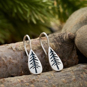 May include: A pair of silver dangle earrings with a tree design. The earrings are in the shape of a teardrop and have a silver hook.