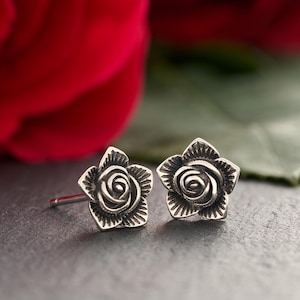 May include: A pair of silver rose stud earrings. The earrings are small and delicate, with a detailed rose design.