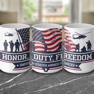 Pode incluir: Caneca de cerâmica branca com um design patriótico. Apresenta a bandeira americana, silhuetas de soldados e helicópteros. A caneca tem as palavras "Honor, Duty, Freedom" e "United States Armed Forces".
