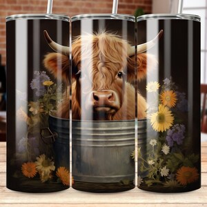 May include: A stainless steel tumbler featuring a Highland cow illustration. The cow is depicted with long, shaggy brown fur, large horns, and is surrounded by colorful flowers. The tumbler has a straw and is designed for cold beverages.
