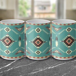 May include: Three white ceramic mugs with a turquoise background and a geometric pattern in shades of red, black, white, and beige. The pattern includes stylized feathers.