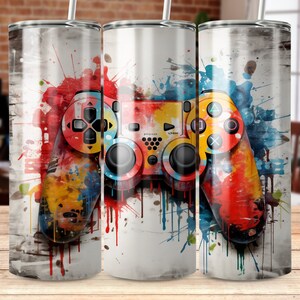 May include: A white tumbler with a colorful paint splatter design featuring a video game controller. The controller is red, yellow, blue, and green.