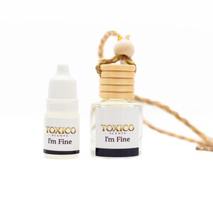 Puede incluir: Dos peque&ntilde;os frascos de vidrio de fragancia "TOXICO SCENTS". Uno es un peque&ntilde;o frasco con cuentagotas, el otro es un ambientador para coche con tapa de madera y cuerda. Ambos frascos tienen el texto "I'm Fine".