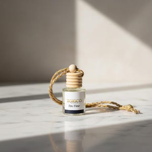 Puede incluir: Peque&ntilde;a botella de vidrio transparente con tap&oacute;n de madera y cuerda dorada y beige. La etiqueta dice "TOXICO I'm Fine" en negro y dorado. La botella est&aacute; dise&ntilde;ada para colgar, probablemente un ambientador o fragancia.