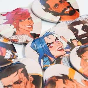 May include: A set of nine heart-shaped badges featuring colourful illustrations of various characters. The badges are made of metal and have a shiny finish.