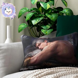 May include: A decorative pillow featuring a shirtless man with silver hair, resting on a bed. The pillow has a dark background with the word "Fere" printed on it. The pillow is on a white couch with a green pillow and a plant in the background.