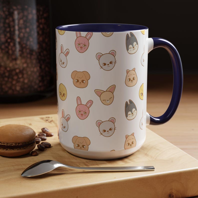 Puede incluir: Una taza de cer&aacute;mica blanca con un borde y un asa azules. La taza presenta un patr&oacute;n repetido de caras de animales de dibujos animados, incluidos conejos, gatos, perros y p&aacute;jaros.