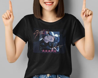 May include: Black t-shirt with a graphic of a person wearing a mask and the text "Stray Kids" in pink and purple lettering. Five pink stars are below the graphic.