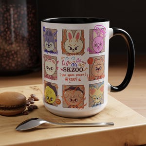 May include: White ceramic mug with a black rim and handle. The mug features a colorful illustration of eight cartoon animals in individual frames. The text "SKZOO" is written in the center of the mug with the text "You make SKZOO stay!" written below it.