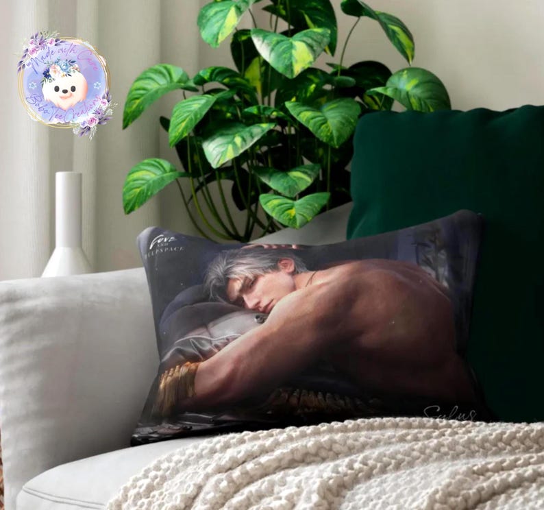 May include: A decorative pillow featuring a shirtless man with silver hair, resting on a bed. The pillow has a dark background with the word "Fere" printed on it. The pillow is on a white couch with a green pillow and a plant in the background.