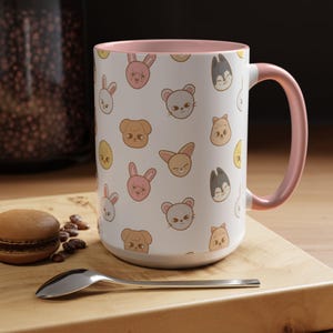 Puede incluir: Una taza de cer&aacute;mica blanca con un borde y un asa de color rosa. La taza presenta un patr&oacute;n repetido de caras de animales de dibujos animados, incluidos conejos, gatos, perros y p&aacute;jaros. Todos los animales sonr&iacute;en y tienen pelajes de diferentes colores.