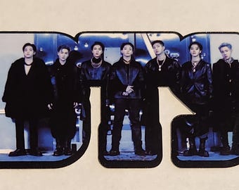 May include: A sticker featuring a group of seven people in black clothing, standing in front of a blue and white background. The word "BTS" is written in large, bold letters across the sticker.