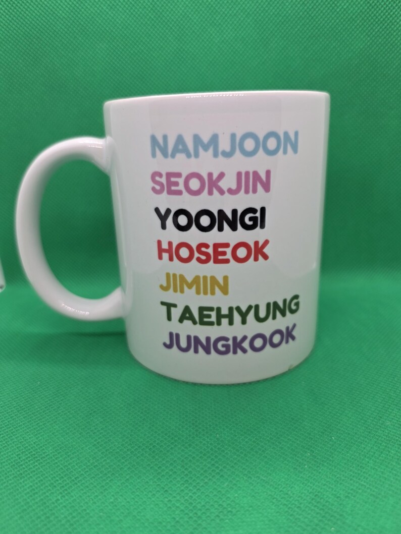 Pu&ograve; includere: Una tazza in ceramica bianca con sette nomi stampati in una colonna verticale in diversi colori: NAMJOON in azzurro, SEOKJIN in rosa, YOONGI in nero, HOSEOK in rosso, JIMIN in giallo, TAEHYUNG in verde e JUNGKOOK in viola.