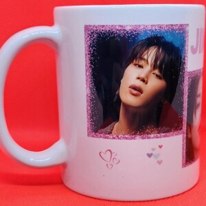 May include: White ceramic mug with a pink glitter border around a photo of a man with dark hair. The photo is surrounded by pink hearts.