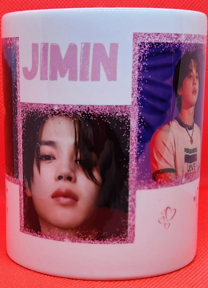 May include: White ceramic mug with a pink glitter design. The mug features a collage of photos of a young man with the word "JIMIN" printed in pink letters.