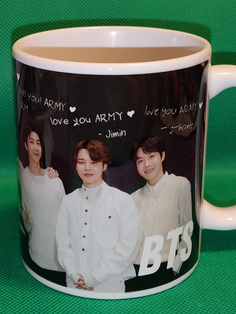 May include: White ceramic mug with a black background featuring a photo of four men. The mug has the text "love you! ARMY" and "love you ARMY" written on it. The text "BTS" is written in large white letters on the bottom of the mug.