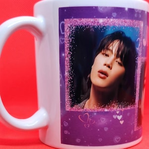 May include: White ceramic mug with a purple background and a pink glitter border. The mug features a photo of a person with dark hair and a light blue shirt. The photo is surrounded by pink hearts.