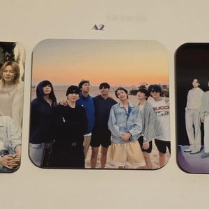 May include: Three square coasters featuring photographs of a seven-member boy band. The first coaster labeled A1 shows the group in light clothing. The second labeled A2 shows them on a beach at sunset. The third labeled A3 shows them in casual attire.