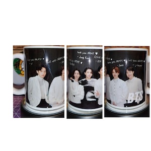 May include: Three white ceramic mugs with black interiors and a black and white photo of a boy band on the front. The mugs have the words "love you ARMY" written on the front, along with the names of the band members.