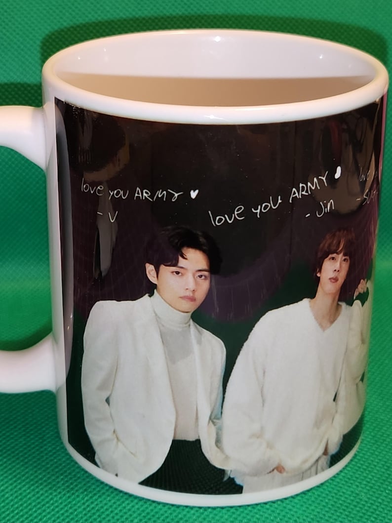 May include: White ceramic mug with a black background featuring a photo of two men in white clothing. The text "love you ARMY" is written on the mug in white, with the names "V" and "Jin" written below.