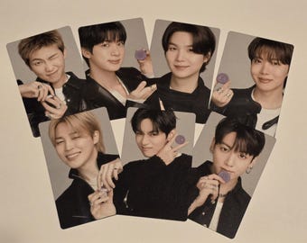 May include: A collection of seven rectangular photo cards featuring portraits of seven individuals. Each person is wearing a dark jacket and holding a small, round, purple object. The individuals are posed against a neutral gray background.