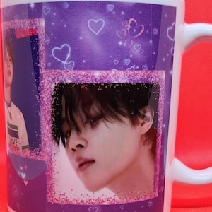May include: White ceramic mug with a purple and pink design featuring a collage of images of a young man with black hair. The mug has a glittery pink border and hearts.