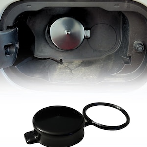 May include: A silver fuel door cap installed in a black compartment, with a black fuel door cap with a black rubber ring below. The fuel door is open, revealing the cap and the fuel door compartment.