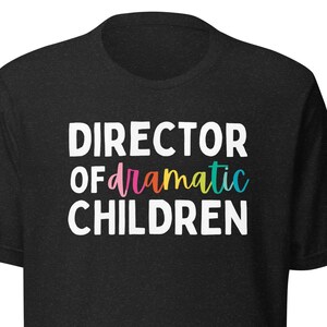May include: Black t-shirt with the text "DIRECTOR OF dramatic CHILDREN" in white with rainbow coloured letters.