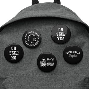 Puede incluir: Una mochila gris con cinco botones negros. Los botones tienen texto blanco que dice "Oh Tech No", "Oh Tech Yes", "What's Said on Headset Stays on Headset", "Stage Managers Never Get Actors to Finally Get Off Book", y "Technically Perfect".