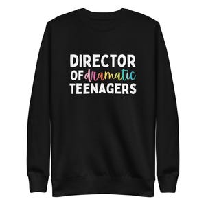 May include: Black sweatshirt featuring the text "DIRECTOR OF dramatic TEENAGERS" in white and rainbow hues. The garment has a crew neck and long sleeves. The text is centrally positioned on the front of the sweatshirt.