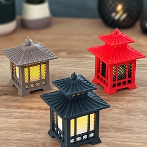 Pode incluir: Três lanternas decorativas com um design asiático tradicional. As lanternas são feitas de plástico e têm um acabamento marrom claro, preto e vermelho. Cada lanterna tem uma pequena luz dentro.