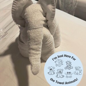 Pu&ograve; includere: Un asciugamano bianco piegato a forma di elefante. Un cerchio blu con il testo "Sono qui solo per gli animali di asciugamano!" e illustrazioni di diversi animali di asciugamano &egrave; in primo piano.