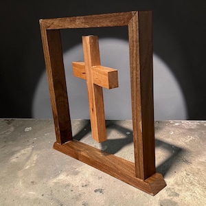 Peut inclure: Sculpture en bois représentant une croix. Une croix marron clair est suspendue dans un cadre rectangulaire marron plus foncé. La croix est en bois plus clair, créant un contraste. Le cadre a une base pour la stabilité.