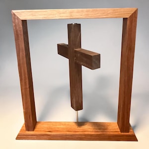 Peut inclure: Sculpture en bois représentant une croix sombre suspendue dans un cadre rectangulaire clair. La base est en bois clair assorti. La croix est fixée à la base par une fine tige métallique.