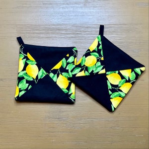May include: Two black pot holders with a lemon print. The pot holders are made of fabric and have a quilted design.