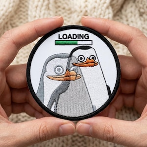May include: Round patch featuring two cartoon penguins with orange beaks and the word "LOADING" above them. The patch has a black border and a white background. The loading bar is green. The penguins are gray and white.